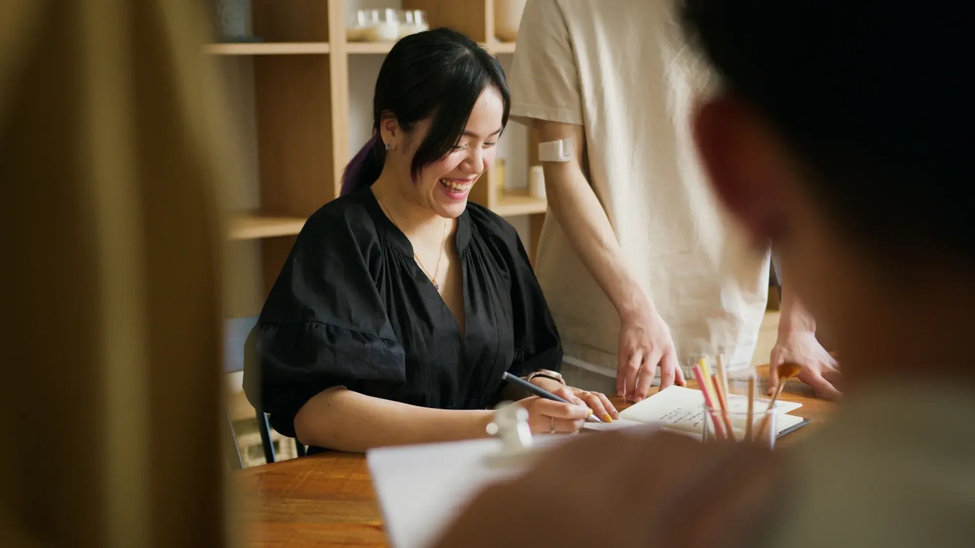 Woman laughing as she takes notes at a table with two colleagues